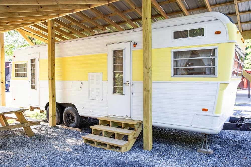 Mellow Yellow vintage camper under a wooden shelter – Mellow Yellow Vintage Camper at The Outpost NRG
